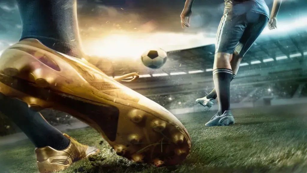 Imagem parcial de dois jogadores de futebol no gramado, com grande plano de chuteiras douradas do que se encontra à esquerda