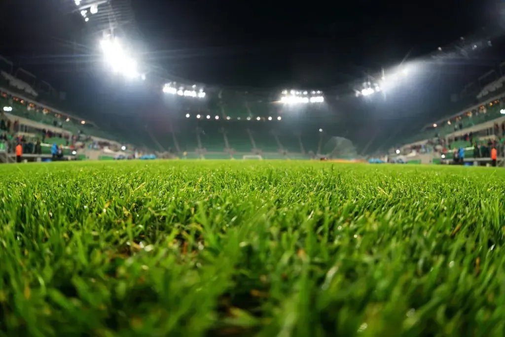 Gramado de estádio, com luzes de arquibancada ao fundo
