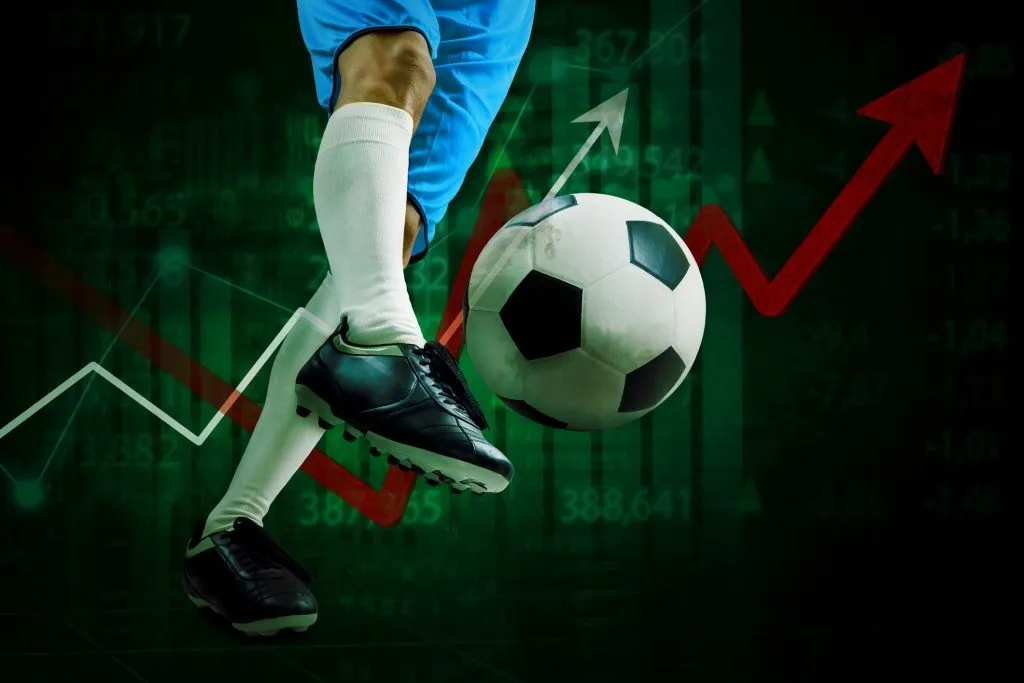 Imagem gráfica das pernas de jogador de futebol, com chuteira preta, meias brancas e short azul, chutando bola de futebol em preto e branco. Ao fundo, um gráfico com setas apontando para cima.