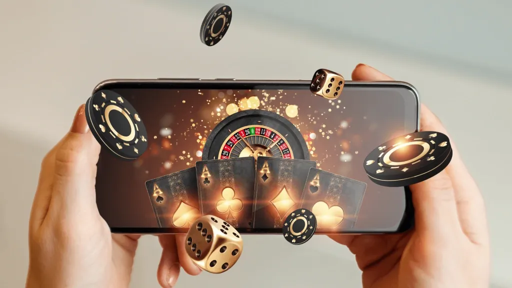 Mãos segurando smartphone com imagem de roleta e cartas de baralho na tela. Algumas fichas de cassino e dados são projetados em 3d para fora da tela. 